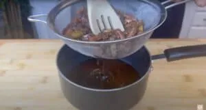 Straining vegetable broth into pot with wooden spoon on cutting board background. Cooking process, kitchen scene.
